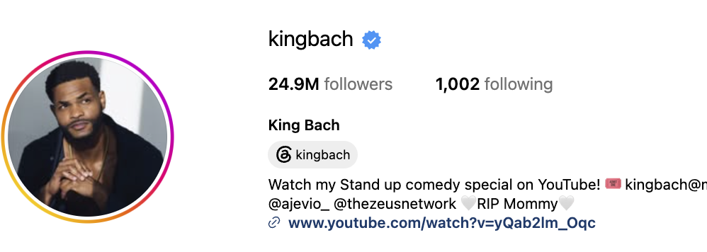 King bach resting one hand on top of the other and staring away from camera in black suit
