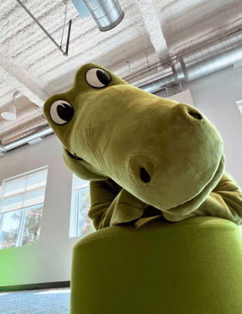 Niles, Crocs’ green crocodile mascot, leaning toward the camera in an office.