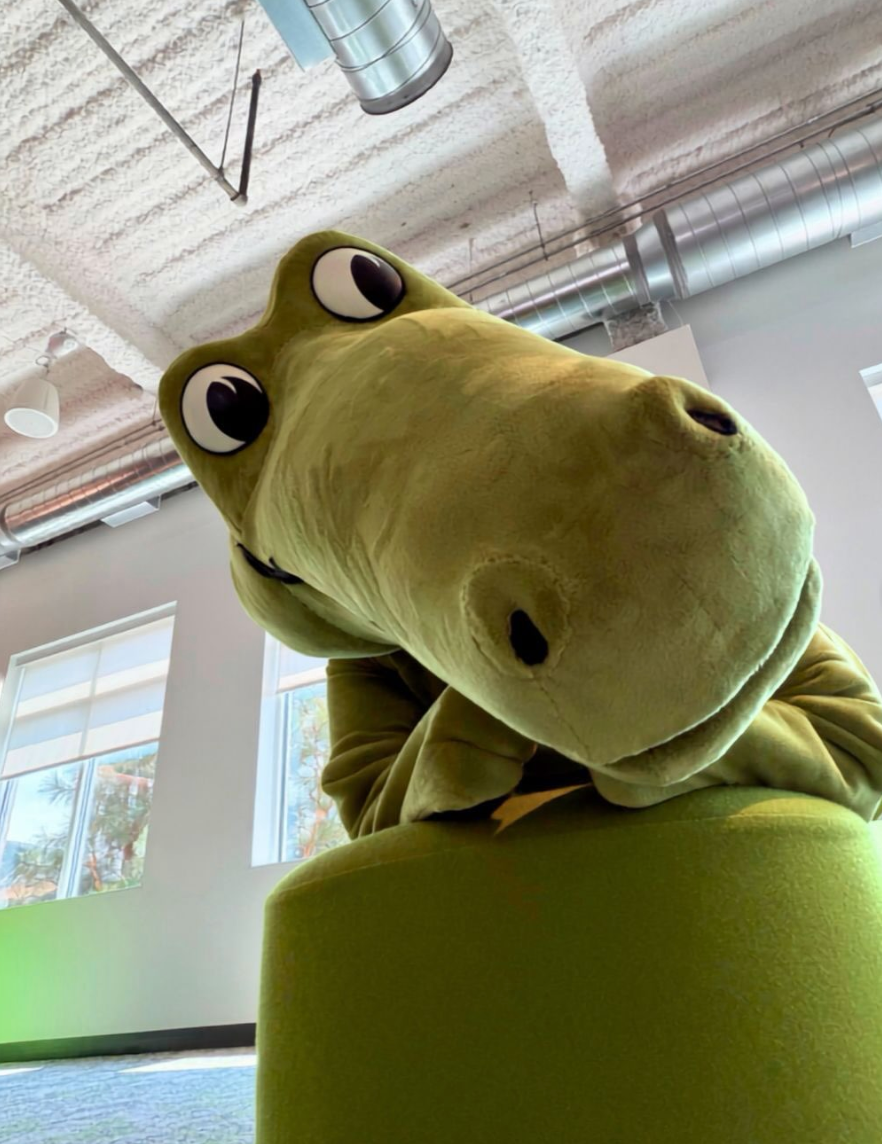 Niles, Crocs’ green crocodile mascot, leaning toward the camera in an office.